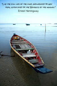 A beached fishing boat rests on the shore of Koh Phangan, Thailand. Quote by Ernest Hemingway.